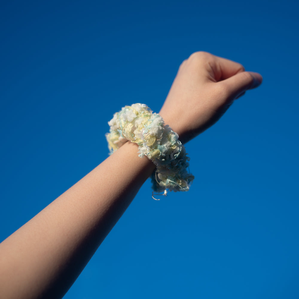 A hand wearing a handmade pastel colour crochet scrunchie made from vibrant Japanese yarns with playful ruffles.