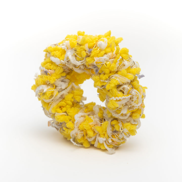 A handmade yellow crochet scrunchie with bead-like yarns resembling mimosa flowers, styled as a vibrant hair accessory.