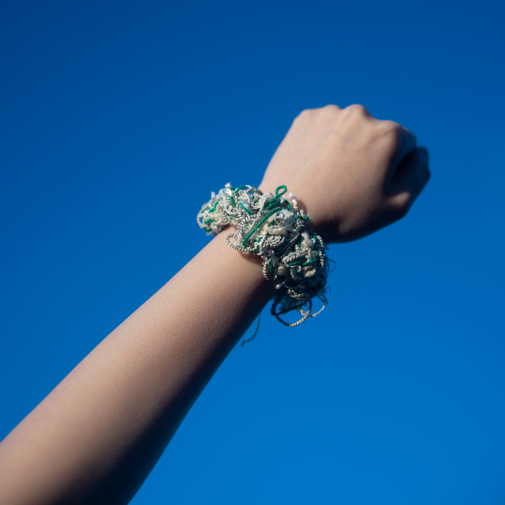 A hand wearing a handmade green crochet scrunchie made from vibrant Japanese yarns with playful ruffles.