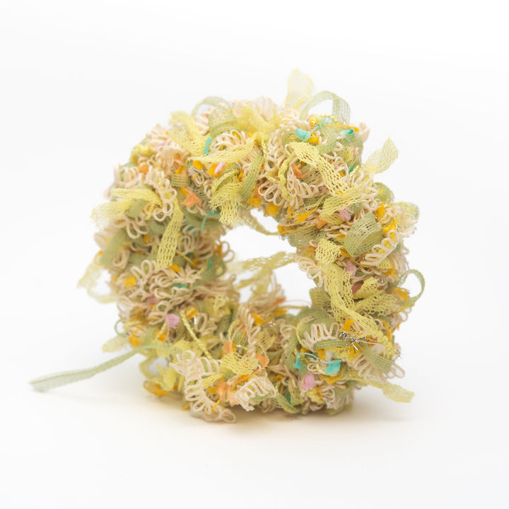 A handmade yellow crochet scrunchie made from light and colourful threads, styled as a vibrant hair accessory.