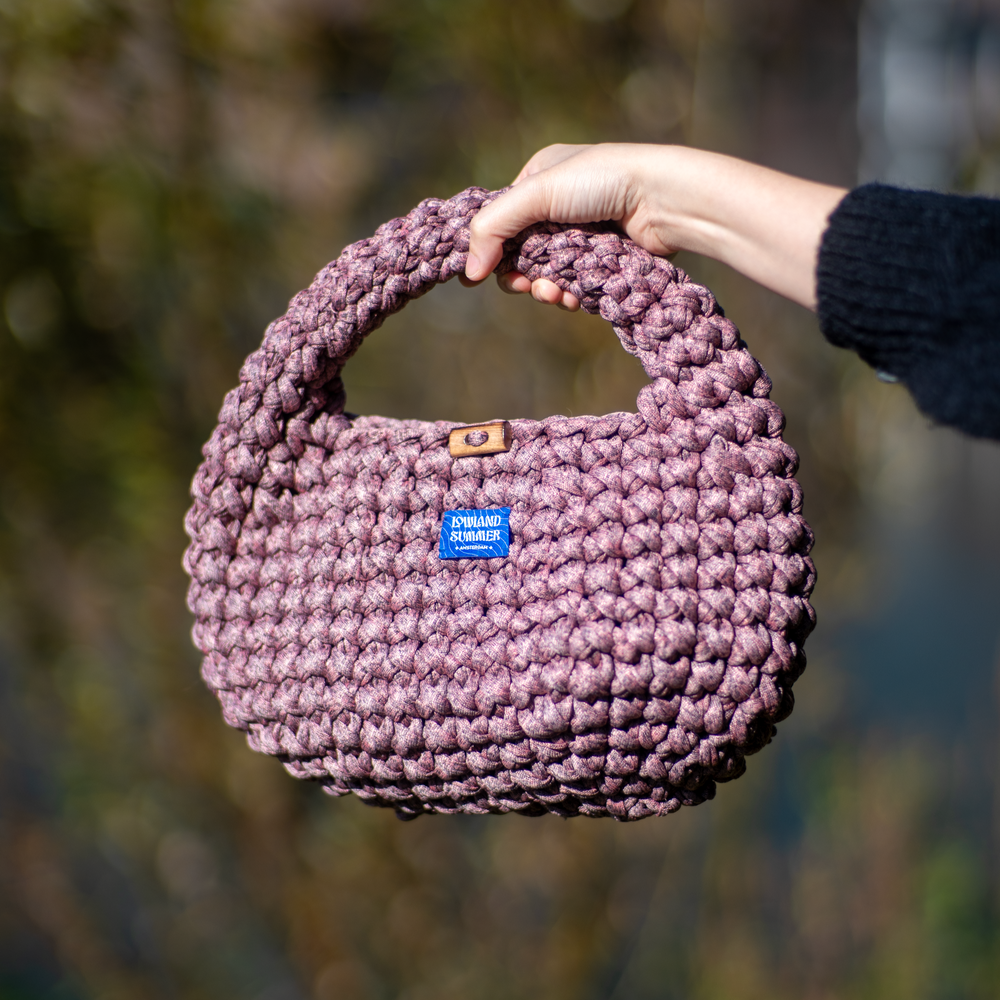 Hand holding a purple knitted bag with a blurred natural background