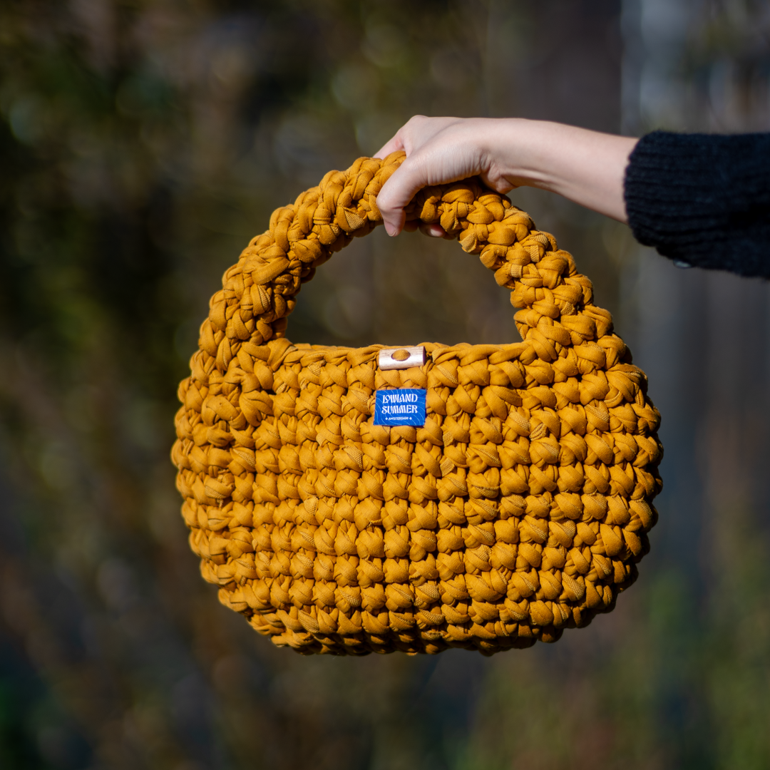 Yellow woven handbag held by a person against a blurred natural background