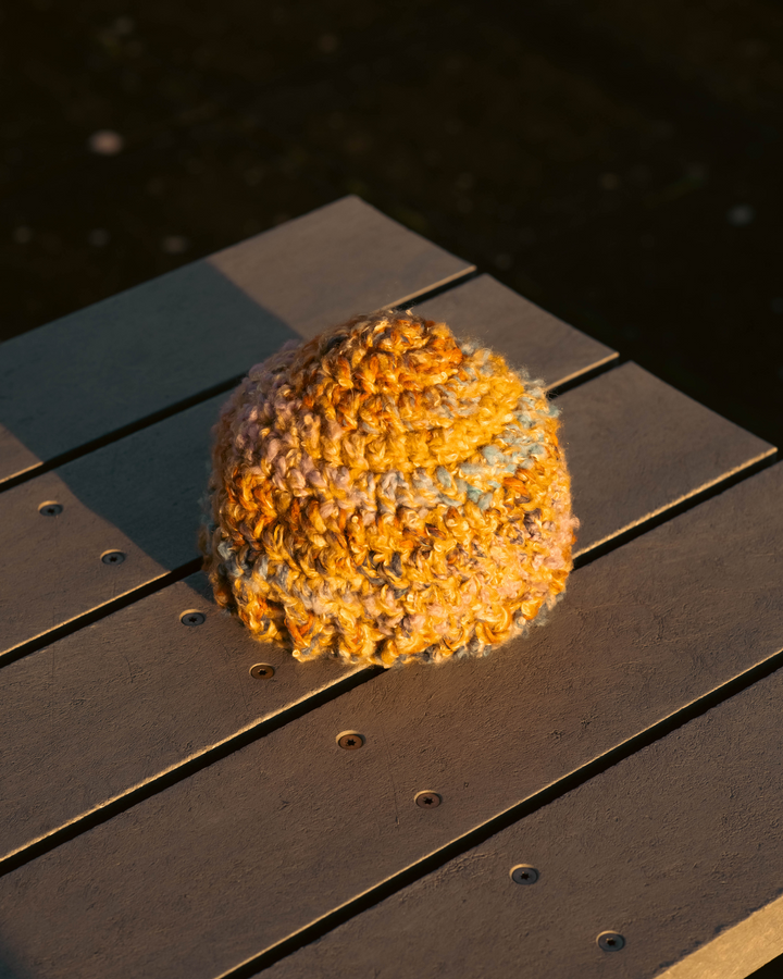 Orange knitted hat on a wooden surface with water in the background