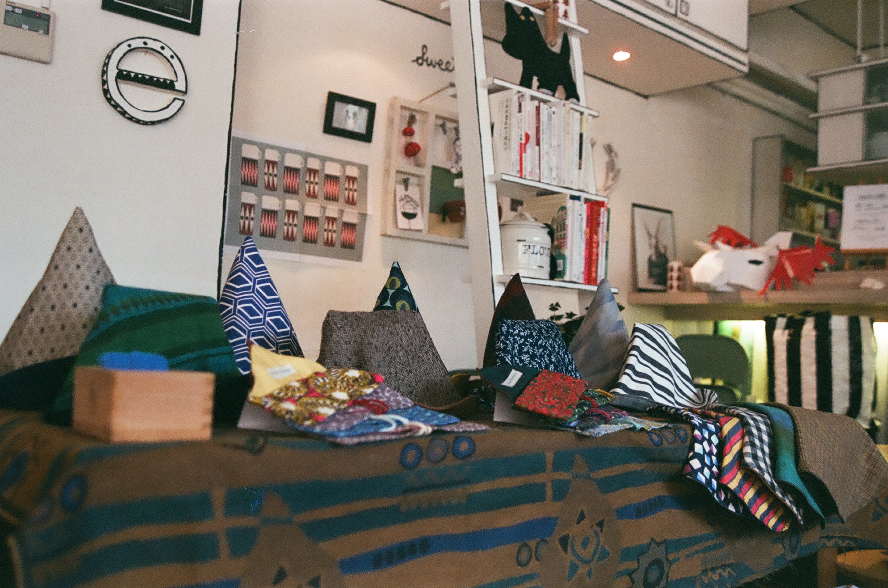 A table in a studio or maker market displaying a variety of colorful handmade hats. The hats are neatly arranged, showcasing different styles, patterns, and vibrant colors, reflecting the artisan's craftsmanship and creativity. The setting suggests a creative space filled with handcrafted items.