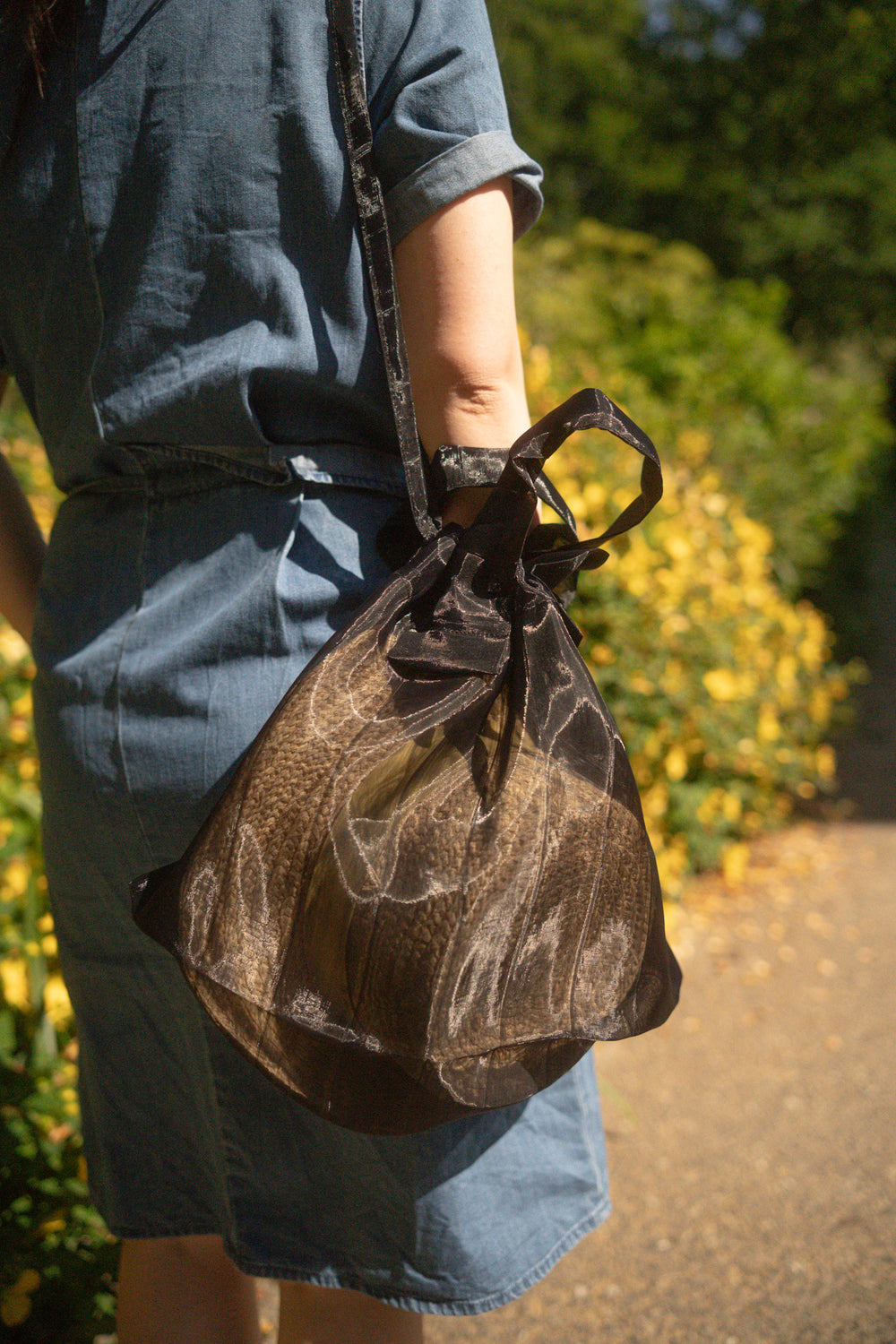 A model wearing a black Japan Mate Mono see-through bag over her shoulder, styled to match her denim dress.