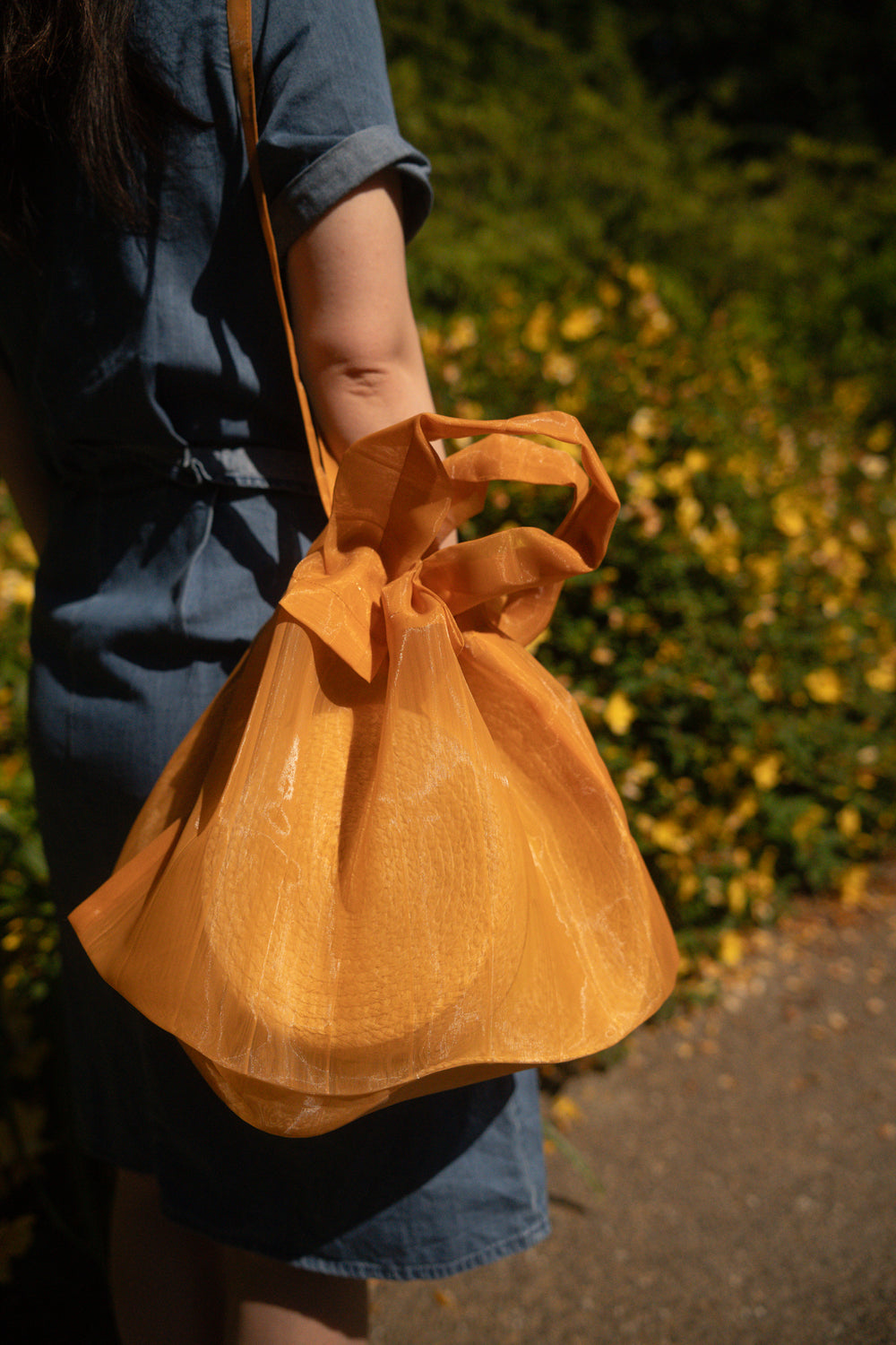 A model wearing an orange Japan Mate Mono see-through bag over her shoulder, styled to match her outfit.