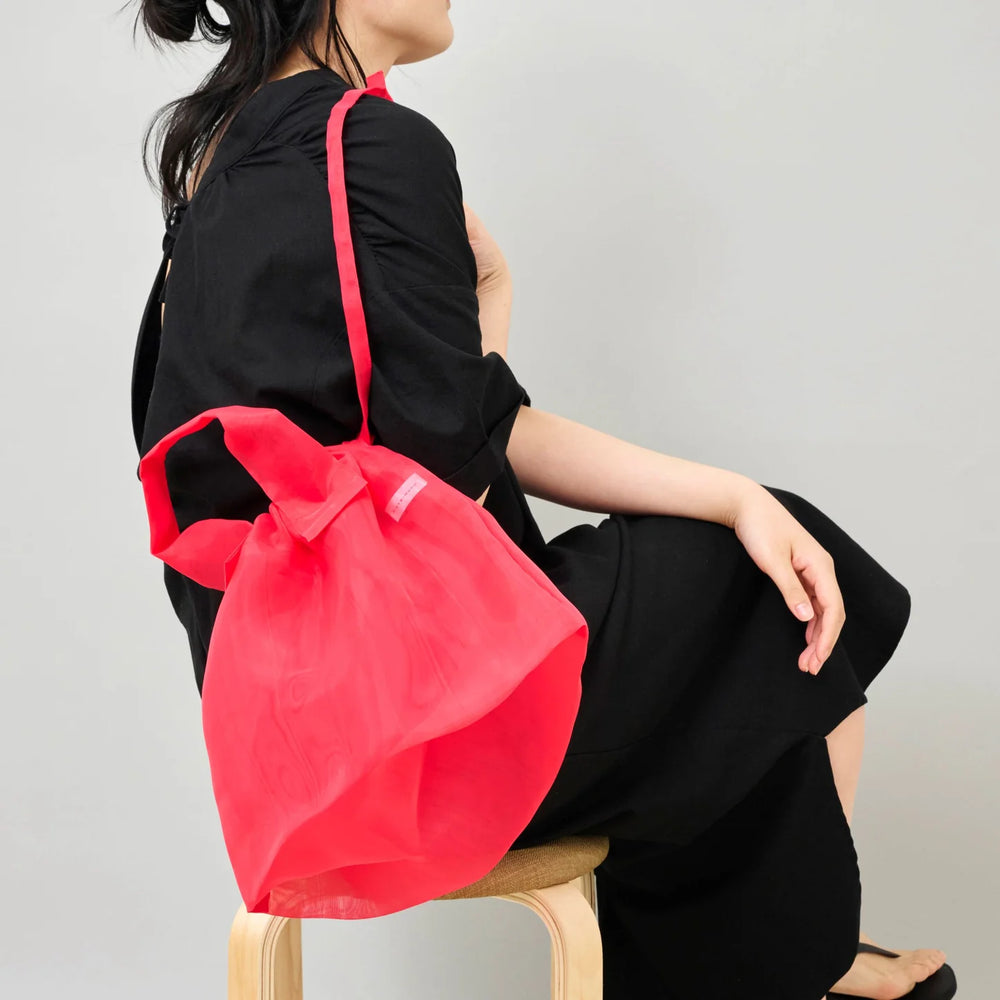 A model carrying a pink Japan Mate Mono see-through bag on her shoulder, styled to match her black outfit.