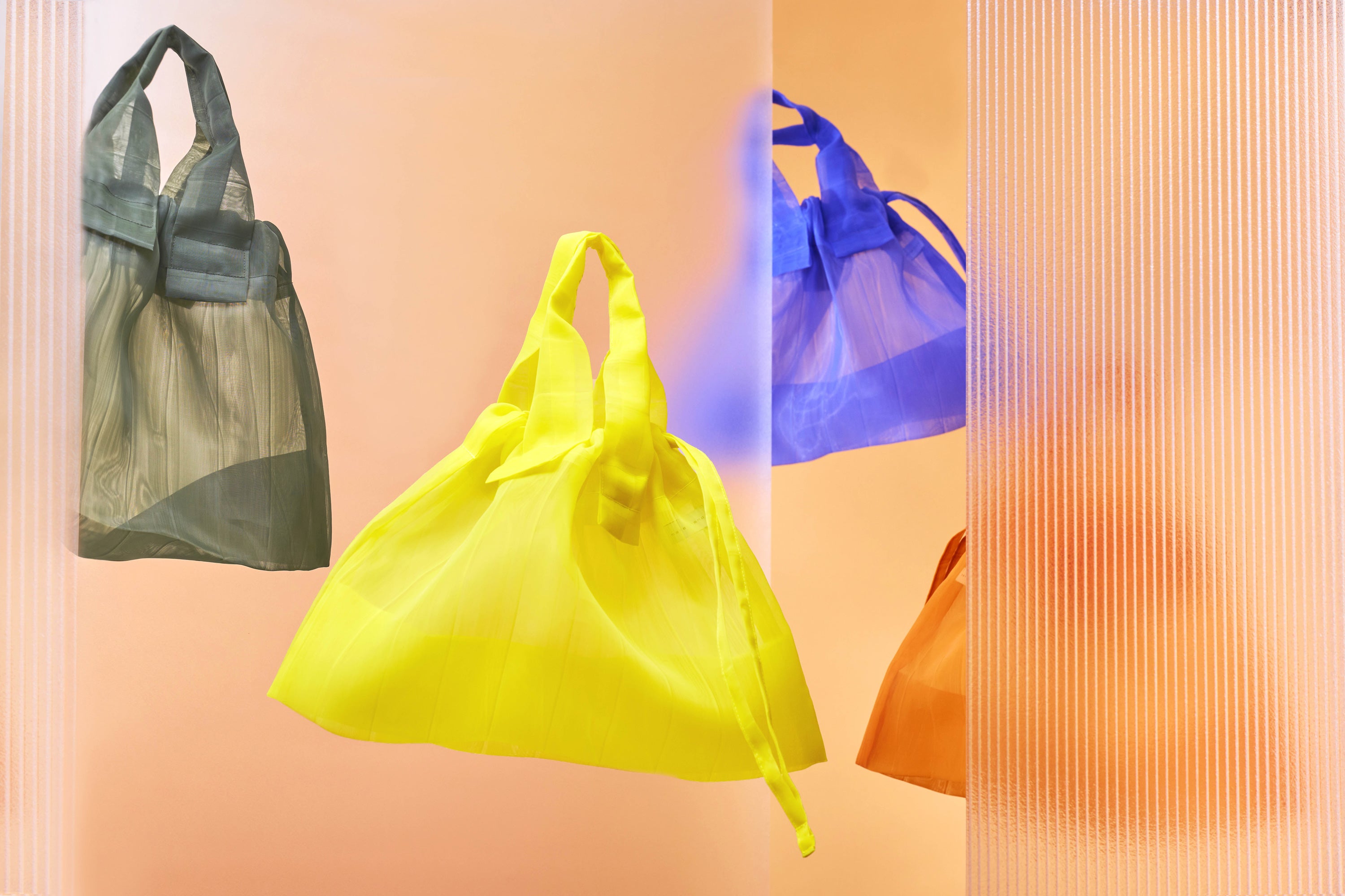 Banner featuring four Japan Mate Mono see-through bags in various colors, stylishly floating against a vibrant orange background.