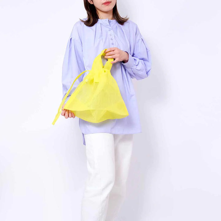 A model holding a yellow Japan Mate Mono see-through bag with her hand, styled to match her purple and white outfit.