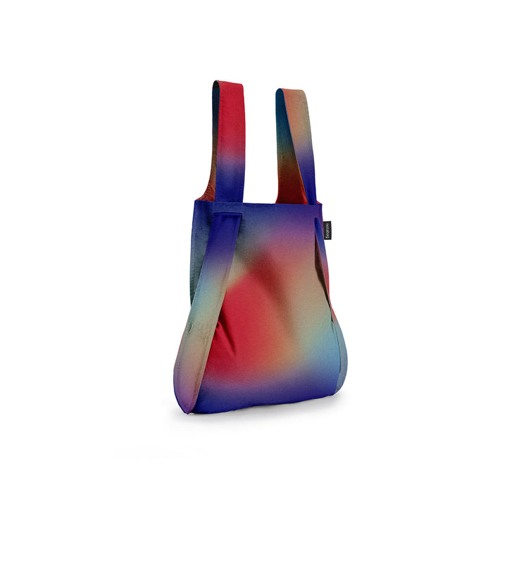 Image of a Notabag displayed in its backpack shape, designed to resemble an aurora with vibrant colours of red, purple, blue, and green, showcasing its versatility and unique design.