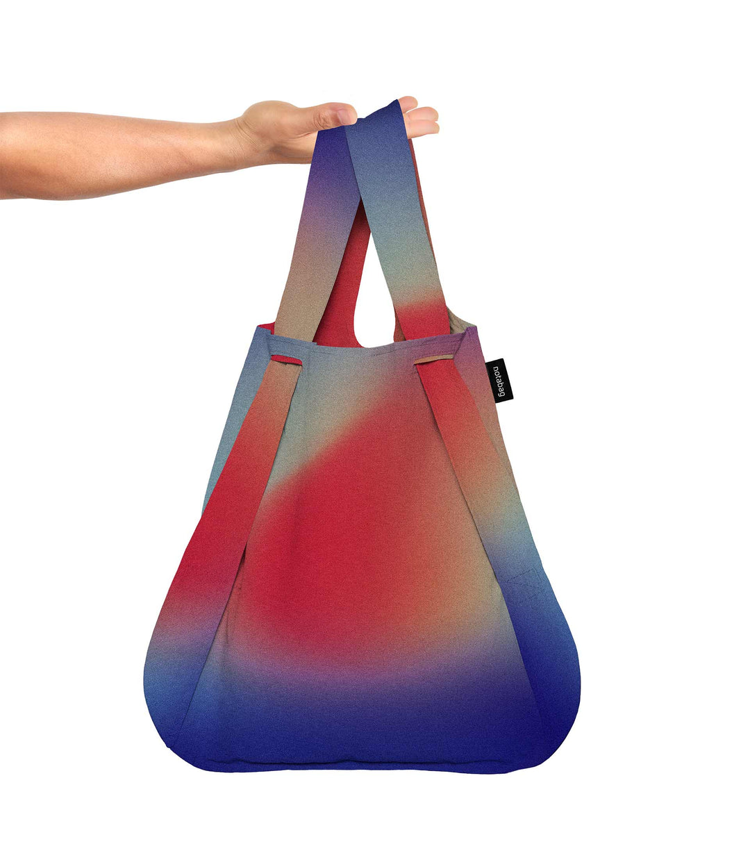 A model holding the aurora Notabag in her hand, showcasing its spacious size and vibrant colours of red, purple, blue, and green.