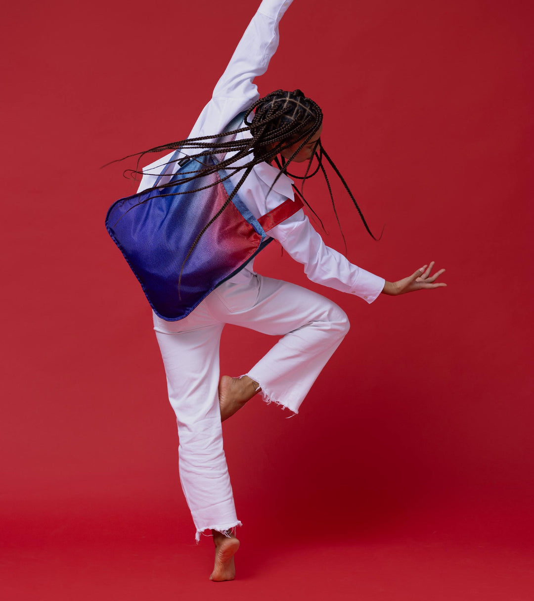 A model wearing the Aurora Notabag as a backpack, dancing joyfully in her white outfit, showcasing the bag's vibrant colors and playful design.