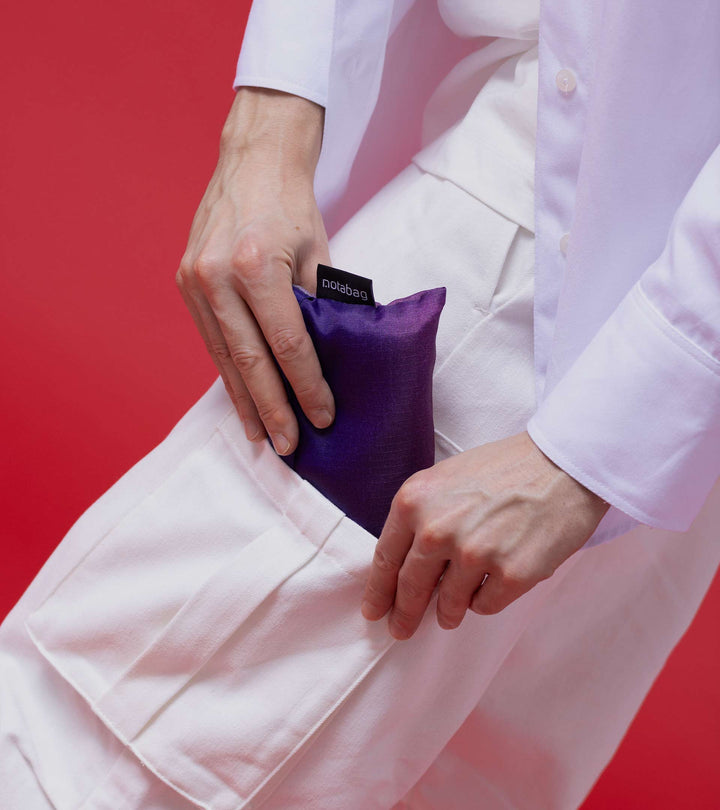 A model taking the folded Aurora Notabag out from the side pocket of her trousers, demonstrating how compact and handy it is for easy access.