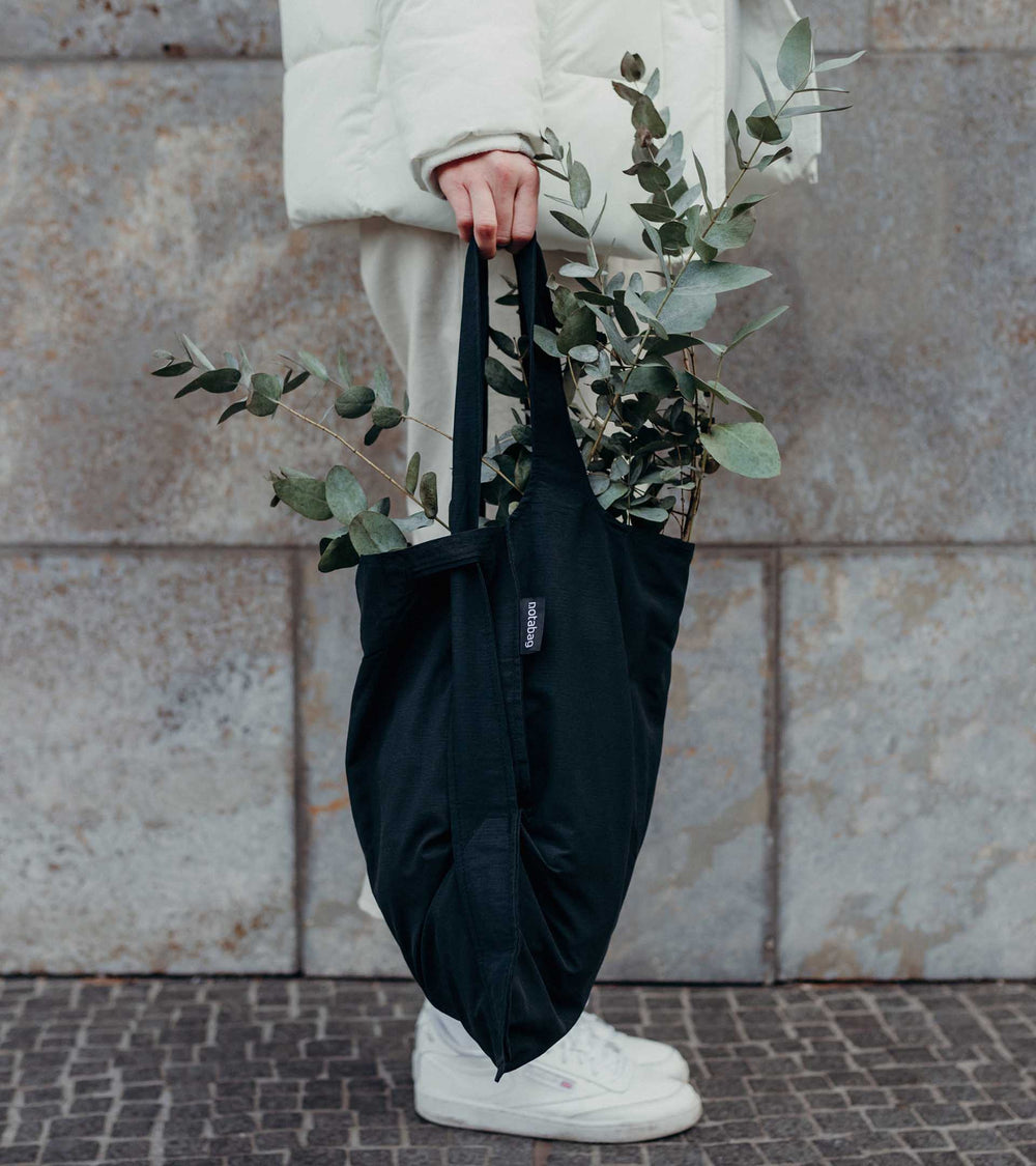 A model holding a black Notabag as a tote bag while buying plants, showcasing its stylish and functional design.