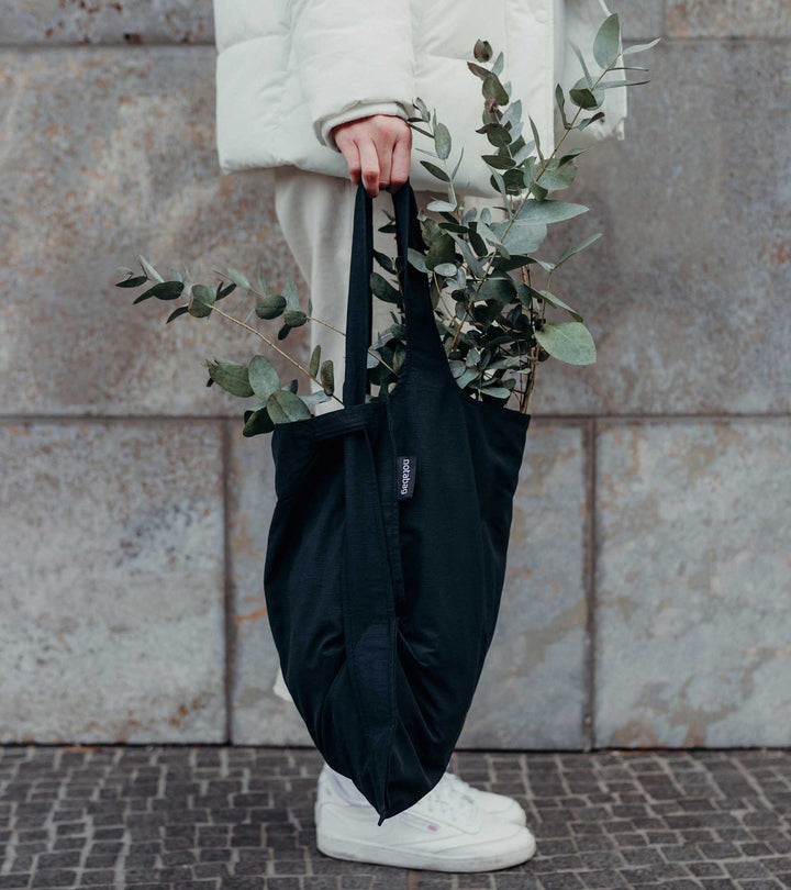 A model holding a black Notabag as a tote bag while buying plants, showcasing its stylish and functional design.