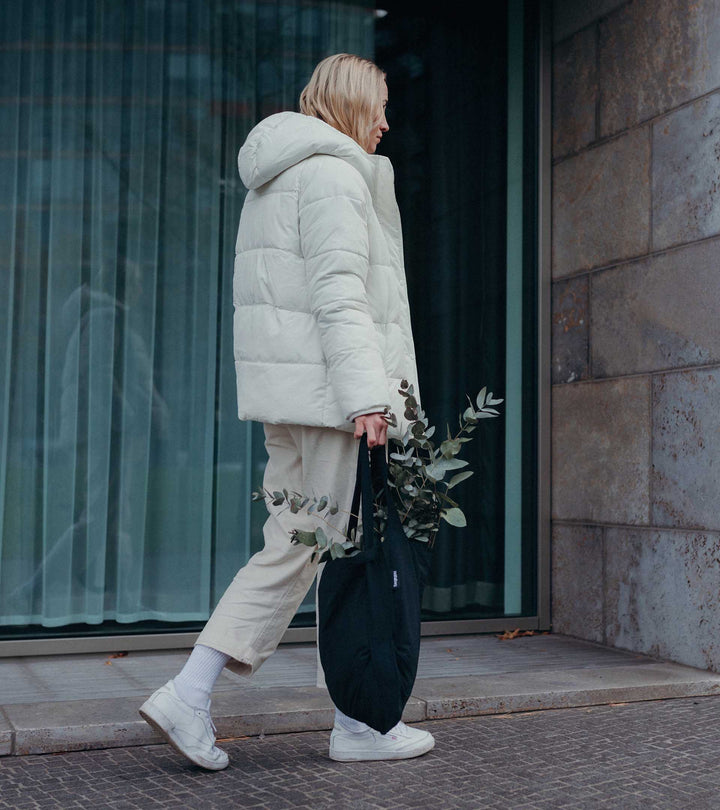 A model holding a black Notabag as a tote bag while buying plants, showcasing its stylish and functional design.