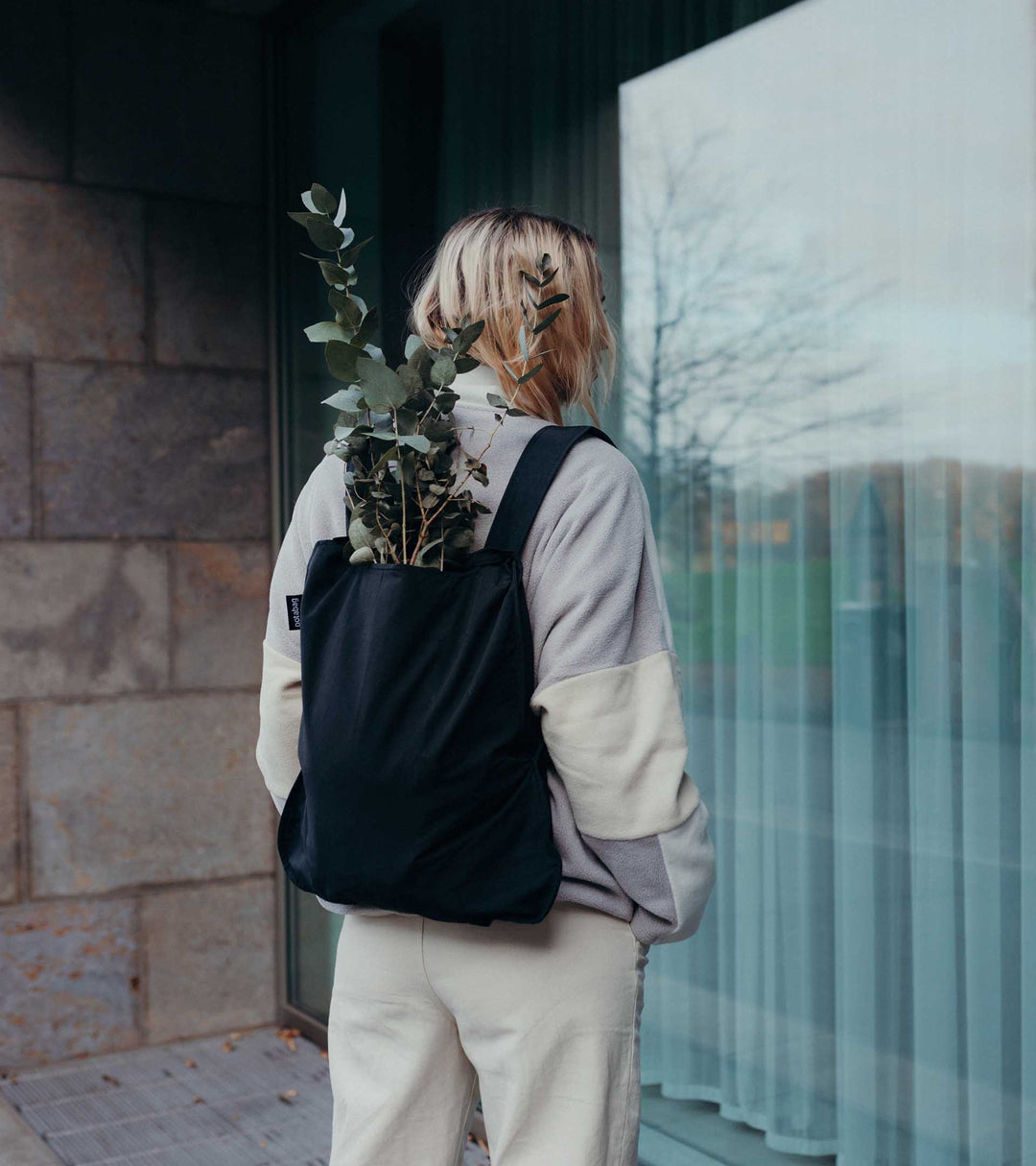 A model wearing a black Notabag as a backpack while shopping for plants, highlighting its versatility and practical design.