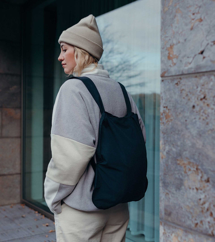 A model wearing a black Notabag as a backpack, styled with her fleece jacket while shopping for plants, showcasing a cozy and practical look.