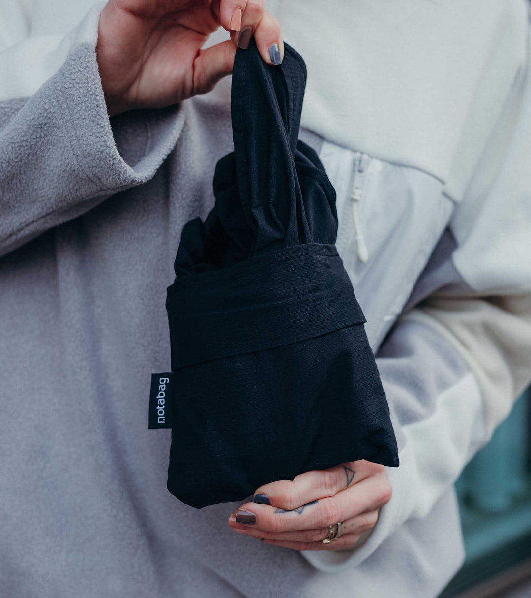 A model folding the black Notabag into a wallet-sized form, demonstrating how compact and handy it is for easy storage and transport.