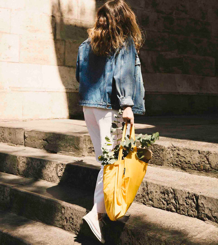 A model carrying the golden yellow Notabag on a sunny day while buying flowers, showcasing its stylish and functional design.