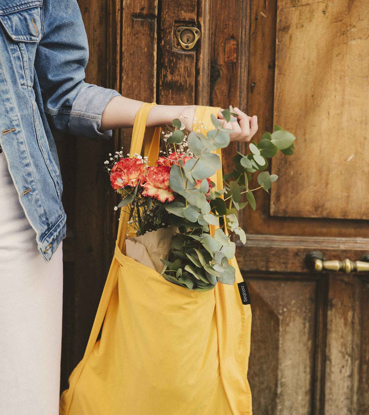 A model carrying the golden yellow Notabag on a sunny day while buying flowers, showcasing its stylish and functional design.