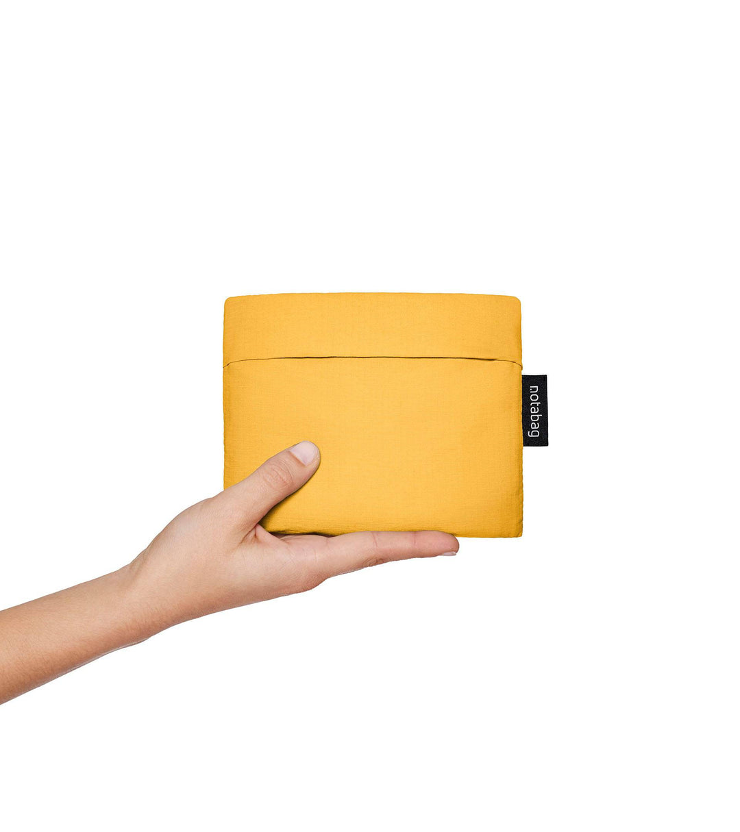 A model holding a folded golden yellow Notabag in her hands, showing its compact size, similar to a wallet. The bag's slim, minimalist design is visible as she begins to unfold it, highlighting its portability and convenience for easy storage.