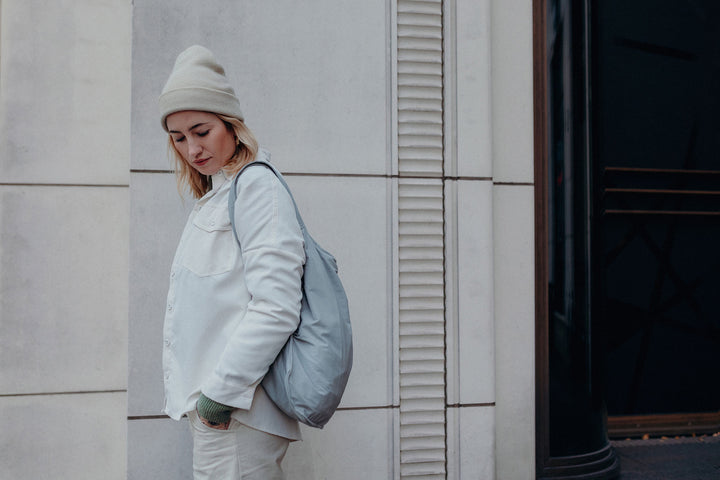 A model wearing the grey Notabag as a backpack, paired with her white winter outfit and a beanie, showcasing a stylish and cozy look.