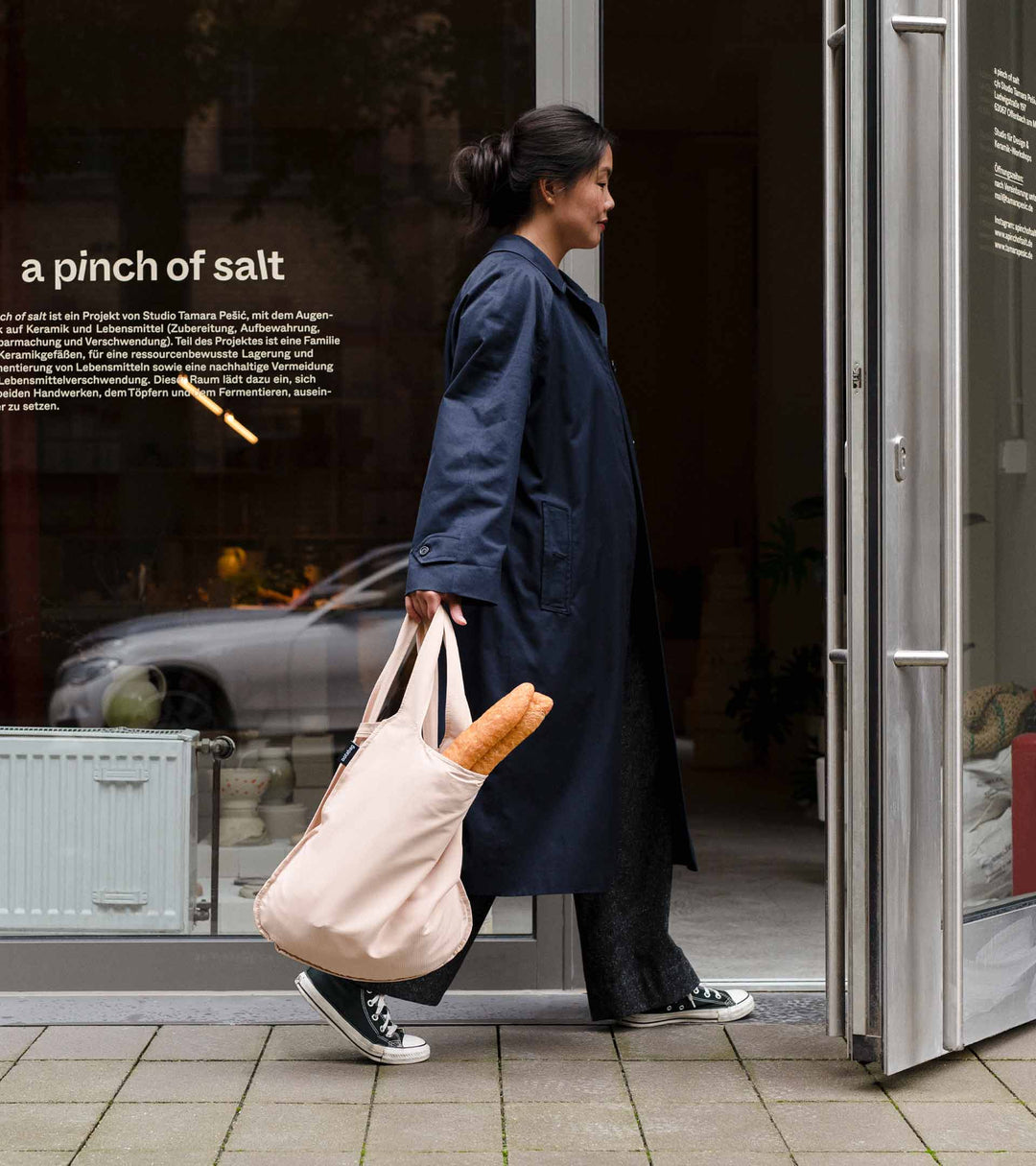 A model carrying a sand beige Notabag with her hand as she enters a shop to do her grocery shopping.