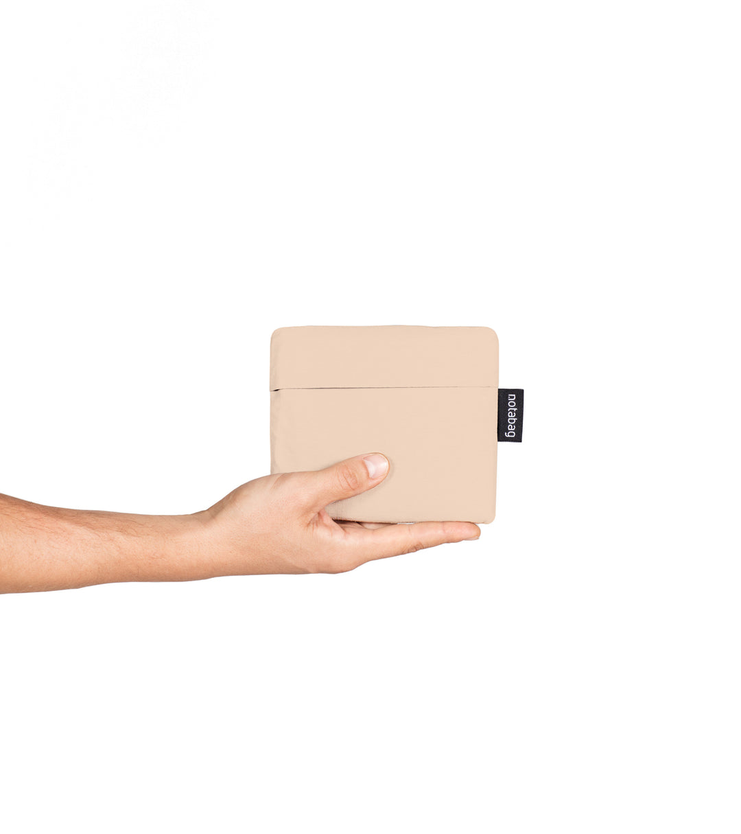 A model holding a folded sand beige Notabag in her hands, showing its compact size, similar to a wallet. The bag's slim, minimalist design is visible as she begins to unfold it, highlighting its portability and convenience for easy storage.