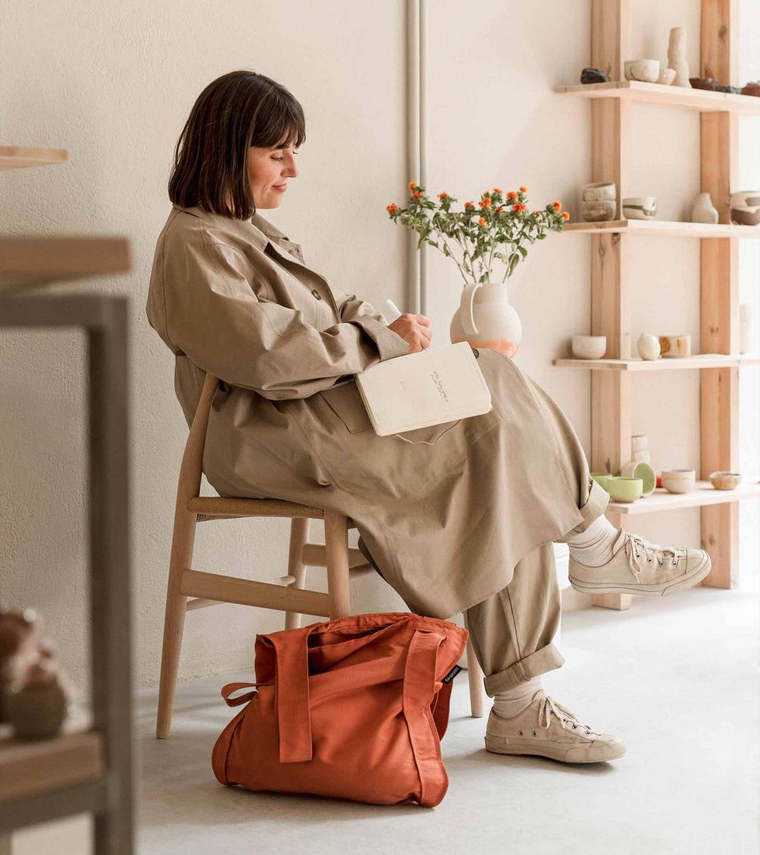 A model sitting in her ceramic studio, writing in her notebook, with a Terracotta Notabag placed on the floor next to her legs, perfectly matching the artist vibe.