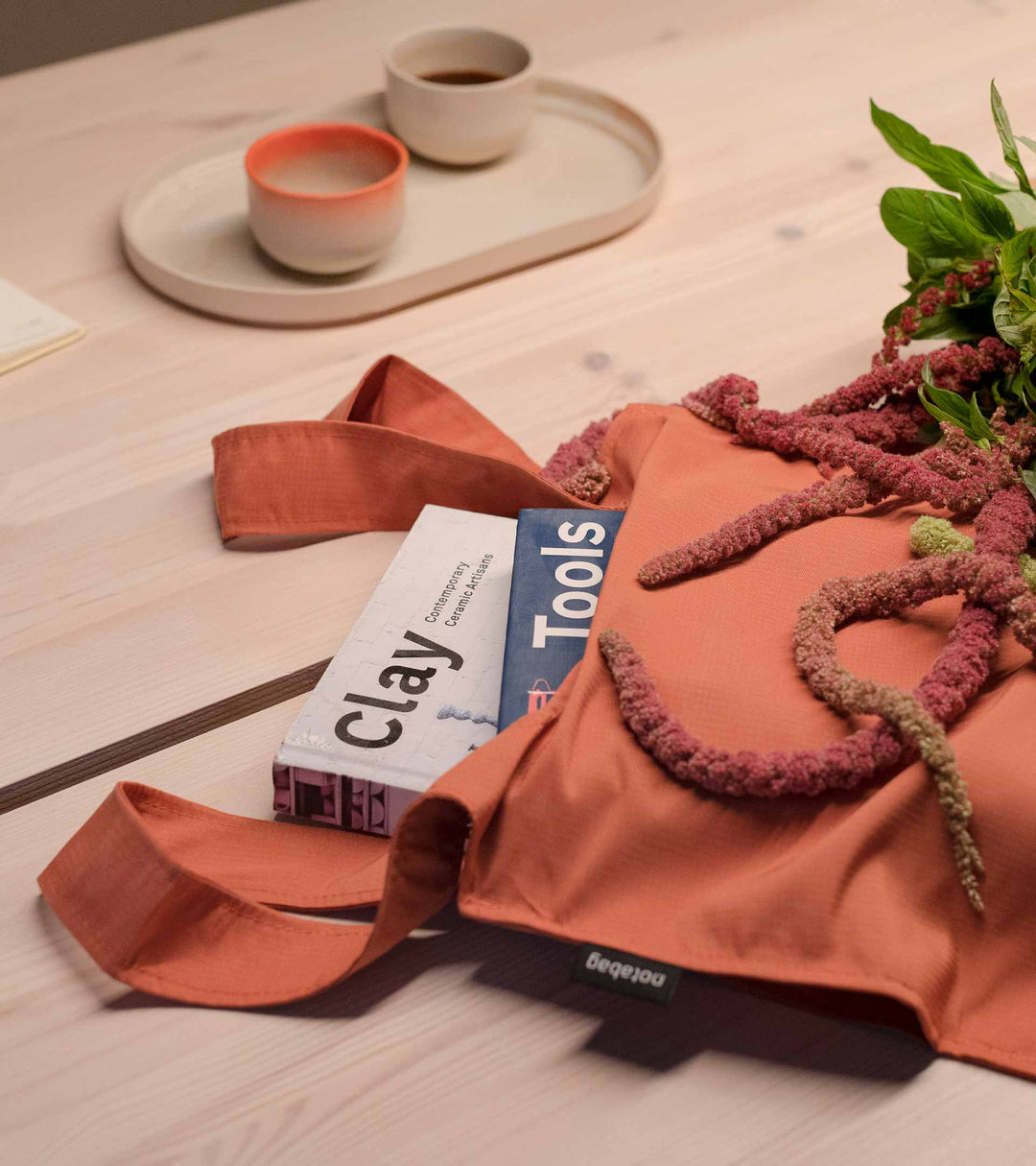 Image of a Terracotta Notabag laid on a desk, with two thick books inside, demonstrating the spaciousness of the bag.