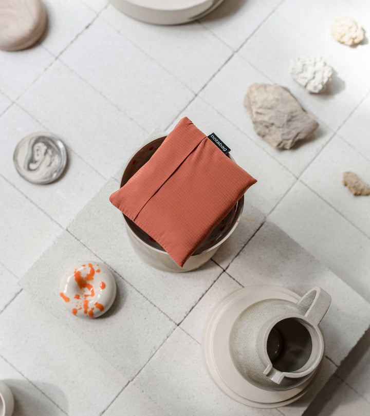 Image of a folded Terracotta Notabag placed on a light white background, accompanied by café utensils to showcase its compact design.