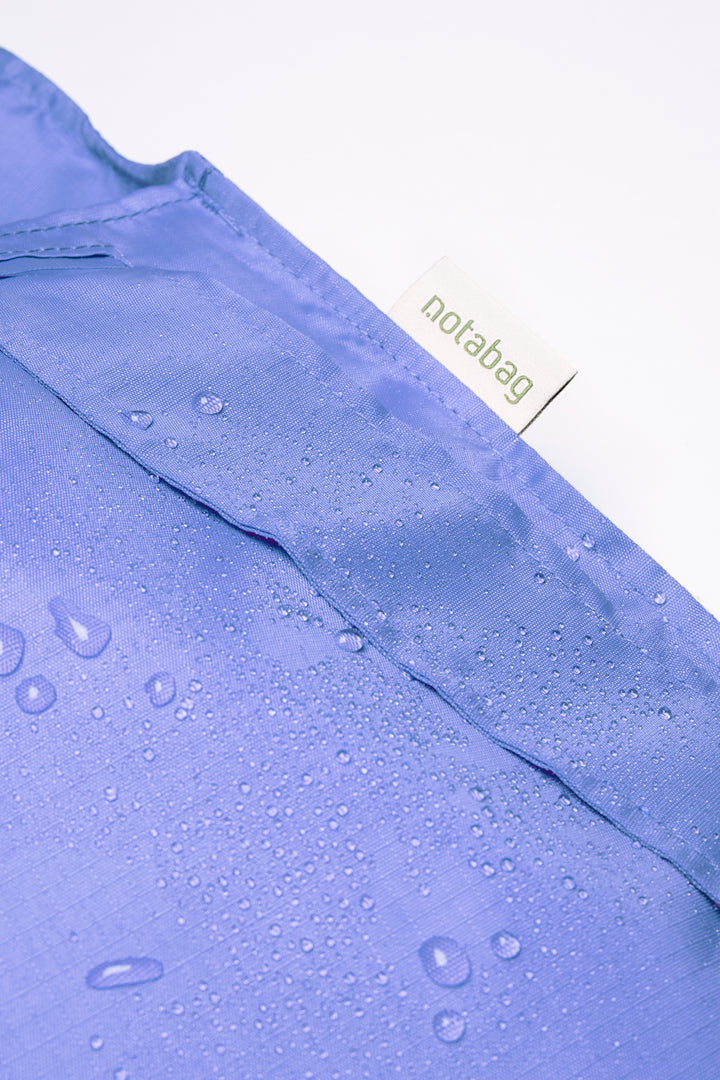 Close-up image of a cornflower purple Notabag featuring water drops on the surface, highlighting its water-resistant quality.