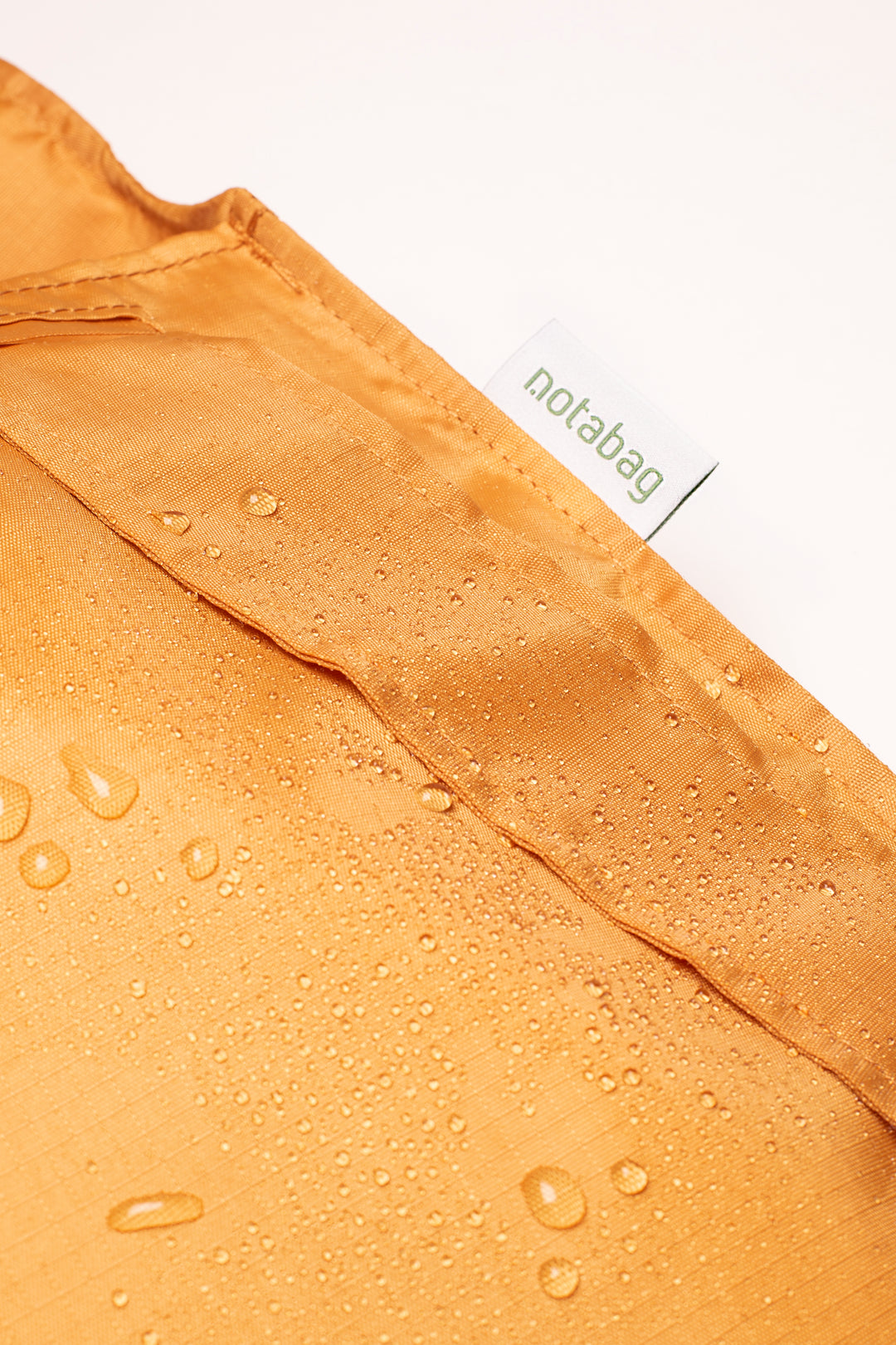 Close-up image of a mustard orange Notabag featuring water drops on the surface, highlighting its water-resistant quality.