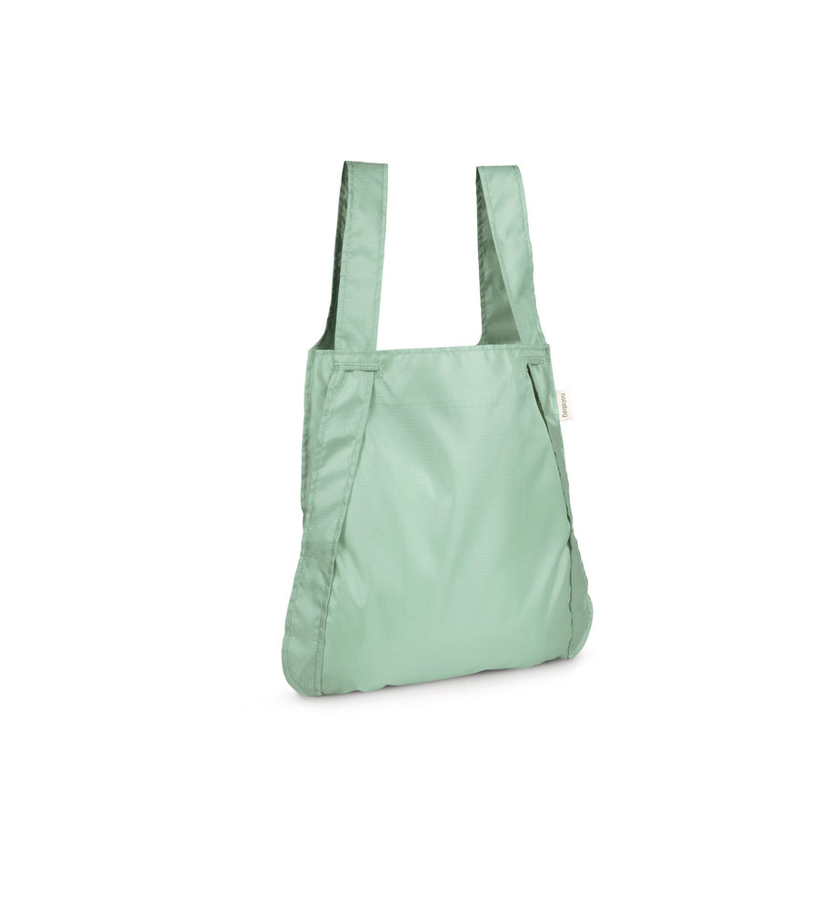 Product shot of a sage green Notabag displayed in its backpack style, highlighting its spacious interior and adjustable straps.