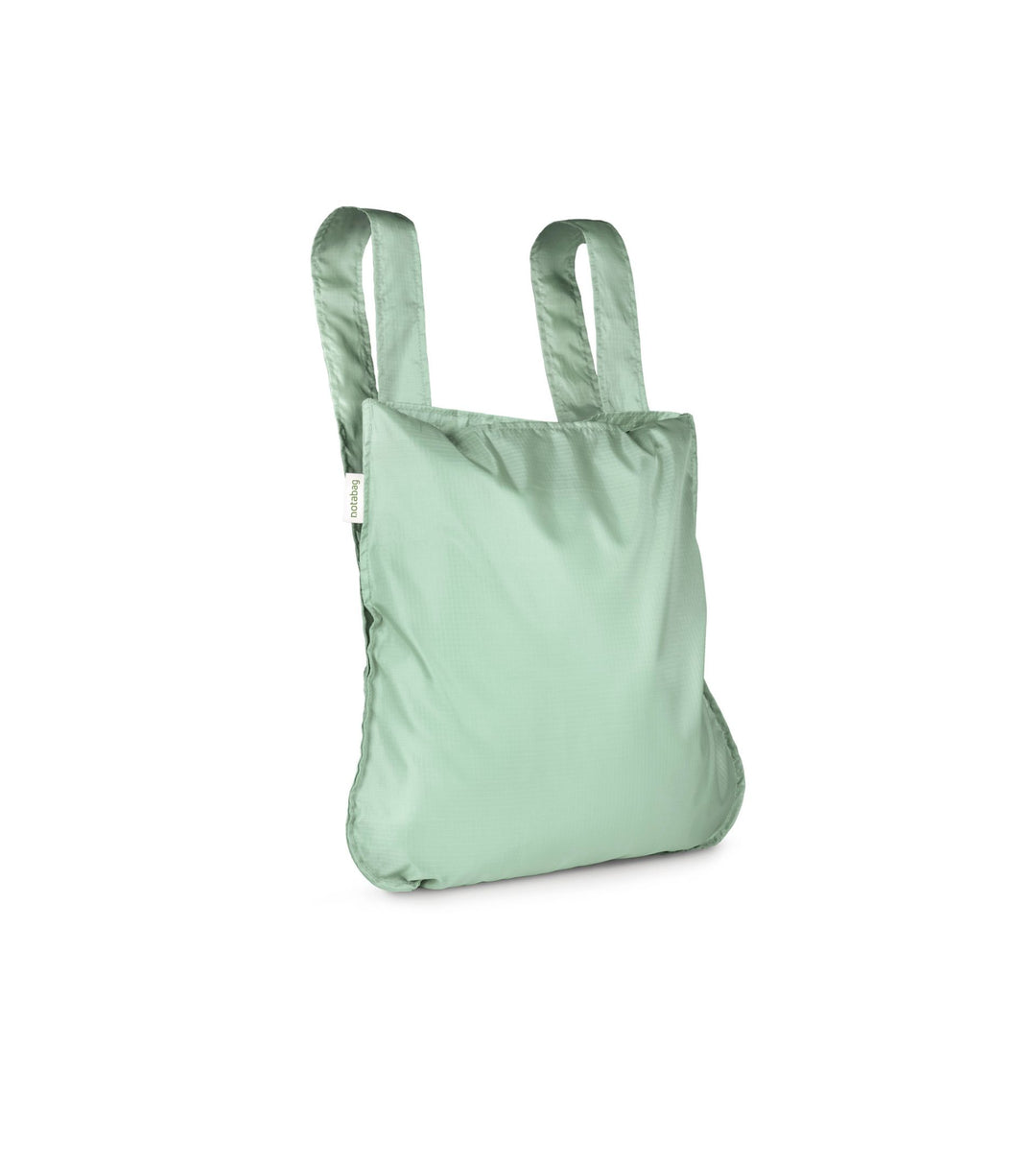 Product shot of a sage green Notabag displayed in its backpack style, highlighting its spacious interior and adjustable straps.