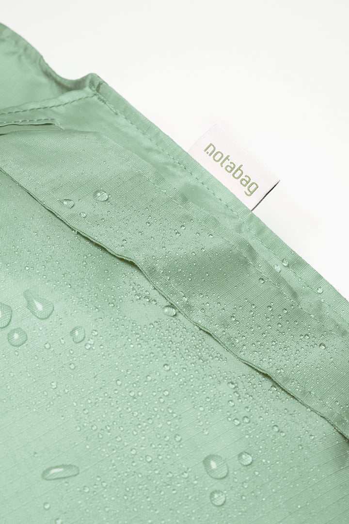 Close-up image of a sage green Notabag featuring water drops on the surface, highlighting its water-resistant quality.