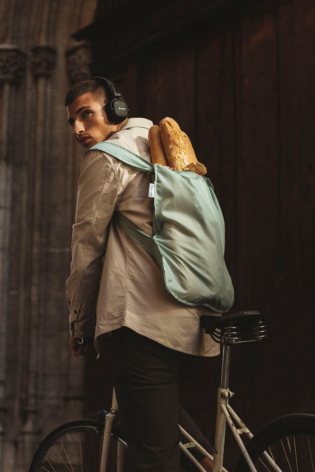 Man riding a bike with a sage green Notabag worn as a backpack, suggesting it's his daily essential for carrying groceries.