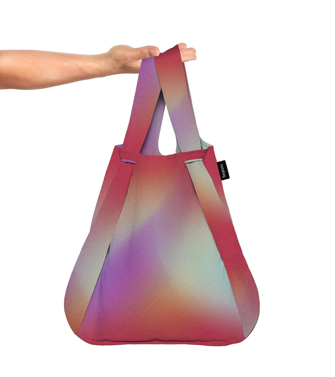 A model holding the sunbeam Notabag in her hand, showcasing its spacious size and vibrant colours of red, purple, orange, and green.