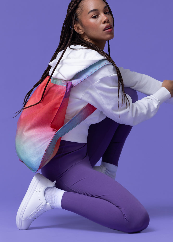 A model kneeling down, wearing a Sunbeam Notabag as a backpack, highlighting its vibrant red and purple colours.