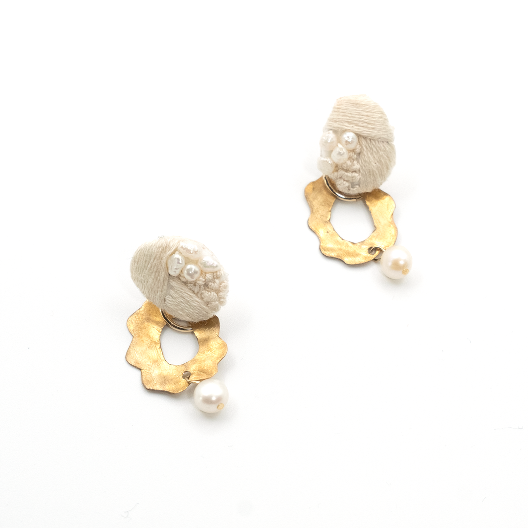 Pair of earrings with gold hexagonal bases and beige spherical elements on a white background