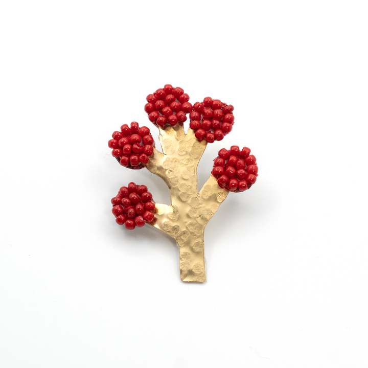 Gold brooch with red berry-like beads on a white background
