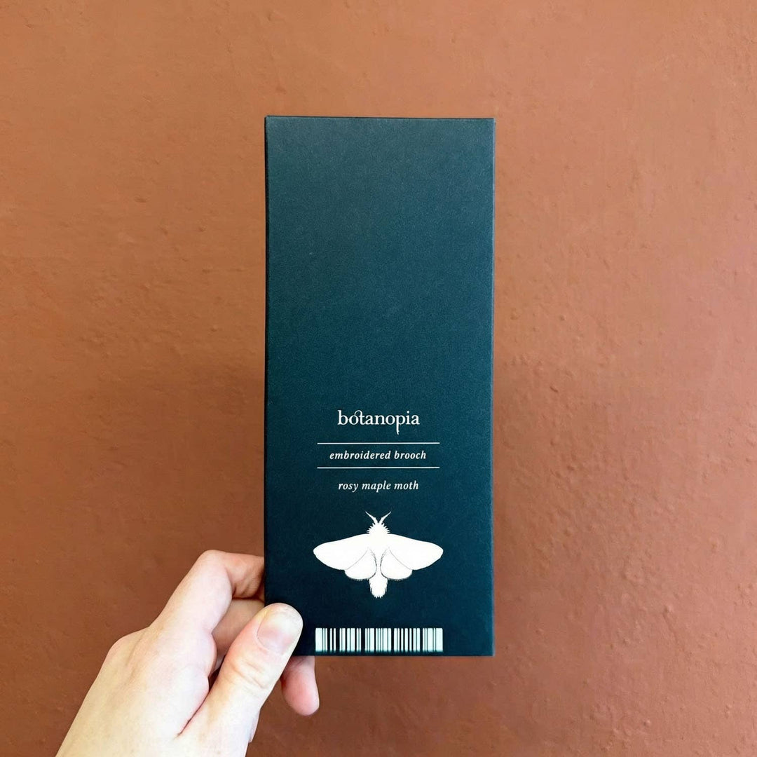 Hand holding a black box with 'botanopia' branding against a brown background