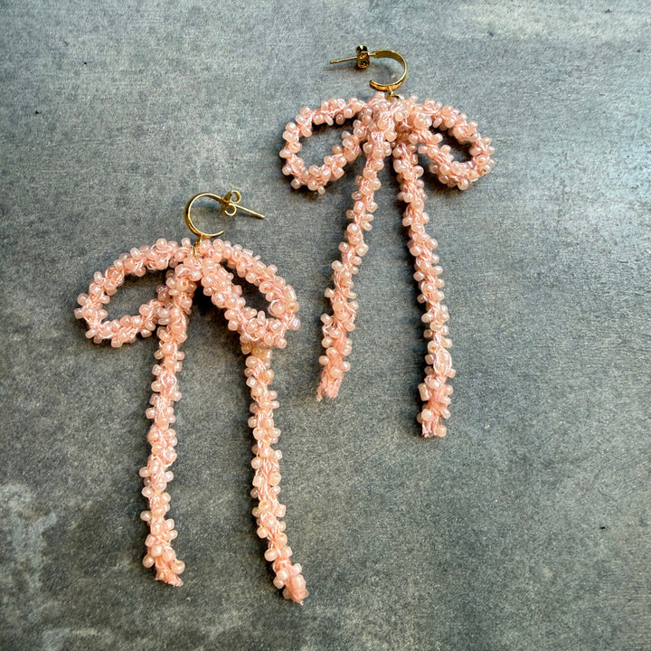 Pair of pink beaded bow earrings on a grey surface