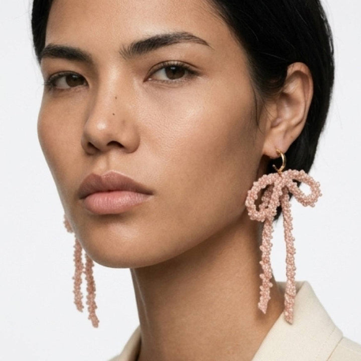 Close-up of a woman wearing pink beaded bow earrings with a neutral background