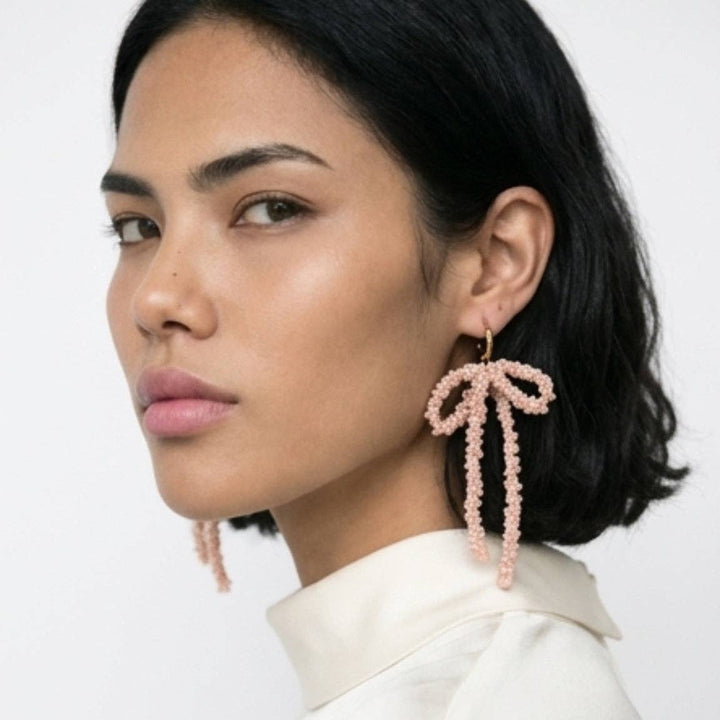 Woman wearing pink beaded bow-shaped earrings on a white background