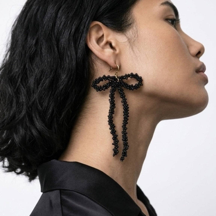 Woman wearing black beaded bow earrings against a neutral background