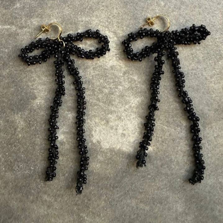 Black beaded bow earrings on a grey surface