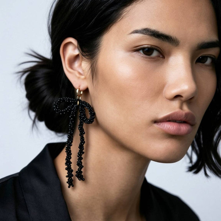 Close-up of a woman wearing black beaded bow earrings against a neutral background