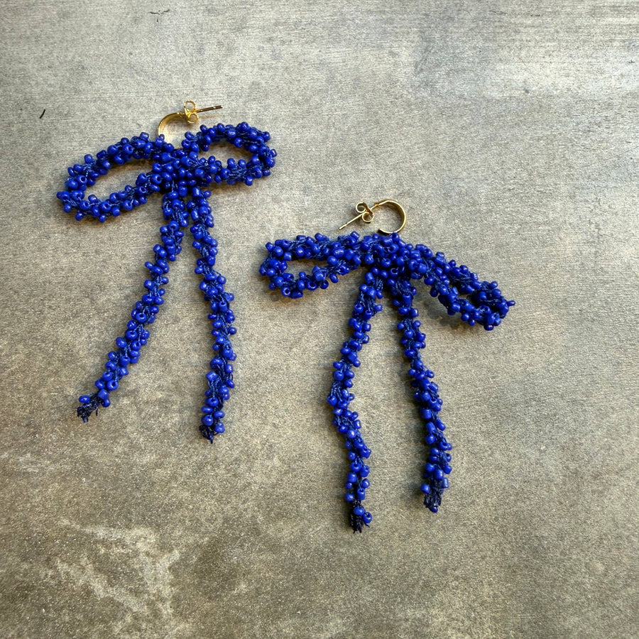 Pair of blue beaded bow earrings on a grey surface